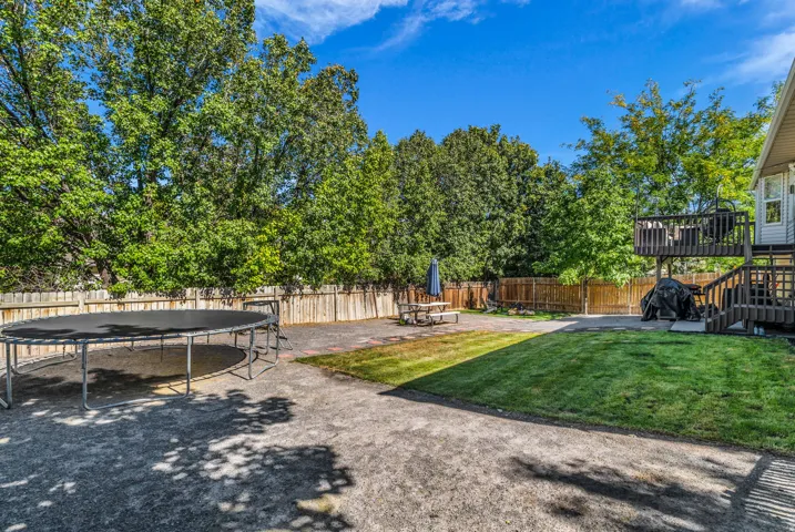 Expansive backyard featuring a manicured lawn, a wooden fence, and mature trees