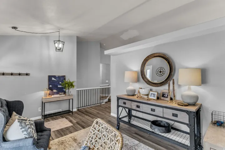 Vaulted ceiling with a suspended light fixture, wood-finish flooring, and a metal railing