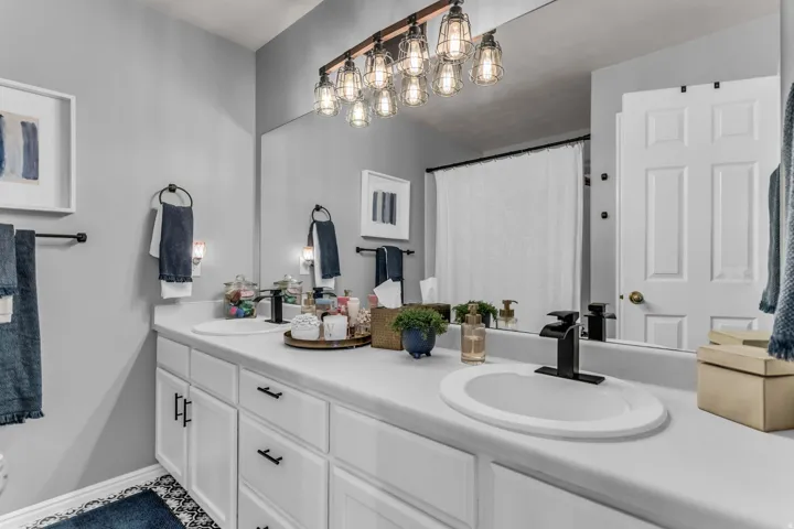 Double vanity with built-in sinks, black finish faucets, white cabinetry, and an expansive wall-mounted mirror