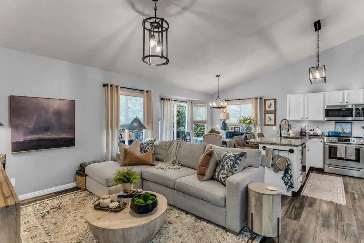 Vaulted ceiling, wood-finish flooring, white cabinetry, stainless steel appliances, and a kitchen island with stone countertop