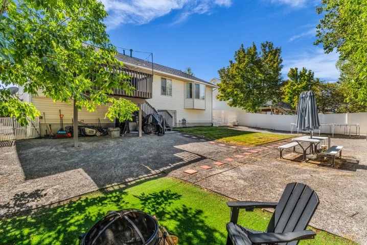 Expansive backyard featuring a multi-level deck, white vinyl fencing, a concrete patio, and mature trees