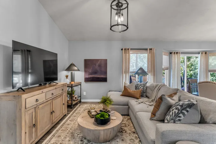 Vaulted ceiling with an industrial-style chandelier, wood-finish flooring, and multiple windows with patio access