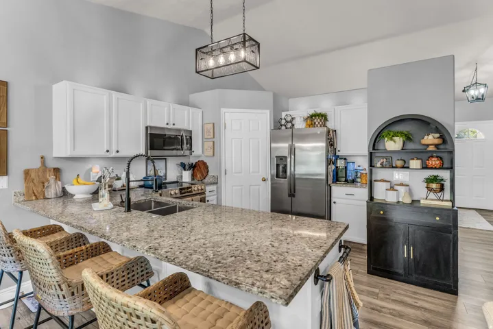 Kitchen featuring an expansive island with a dual basin sink, white cabinetry, stainless steel appliances, and wood-finish flooring