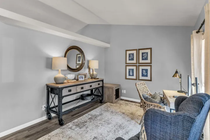 Vaulted ceiling with exposed beams, wood-finish flooring, and light gray wall tones