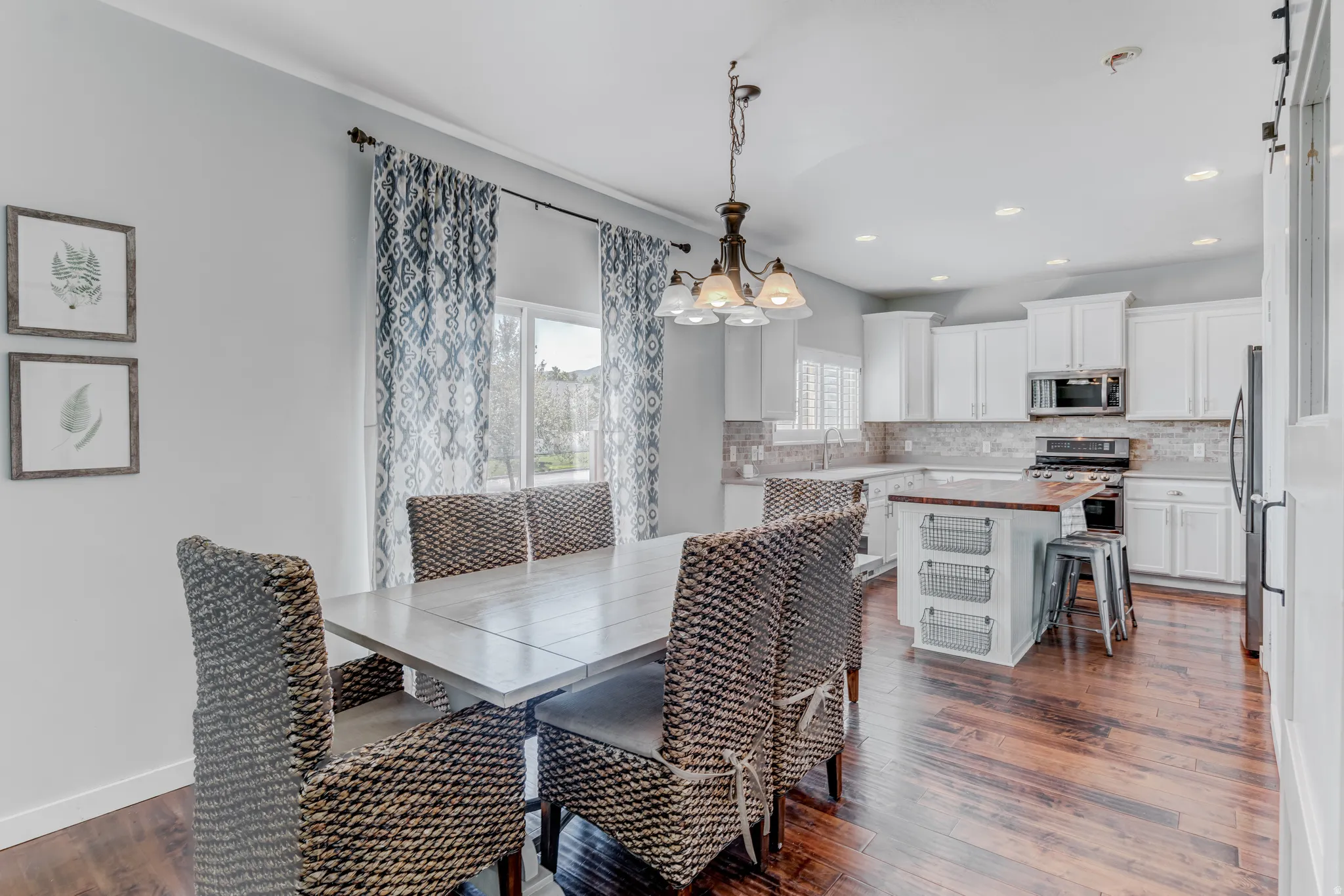 Wood-finish flooring, white cabinetry, integrated stainless steel appliances, recessed lighting, and a kitchen island with a wood countertop
