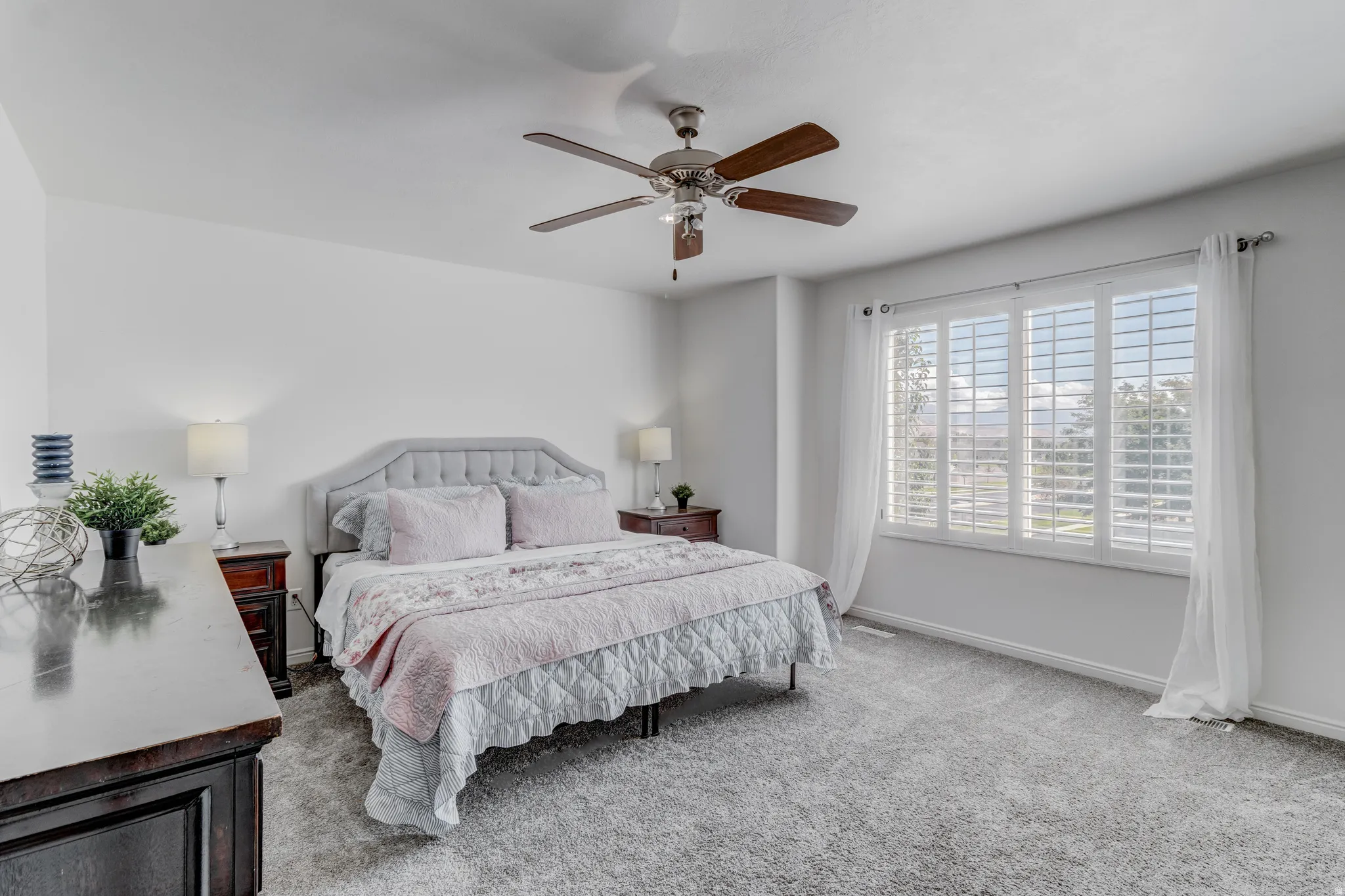 Carpeted flooring, window with plantation shutters, ceiling fan, and white walls