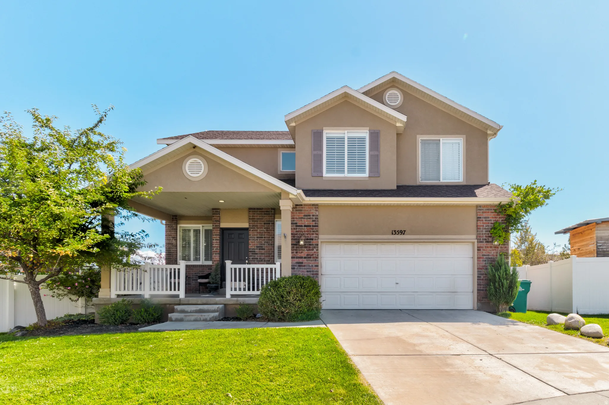Two-story stucco and brick exterior featuring a covered front porch, white garage door, and a concrete driveway