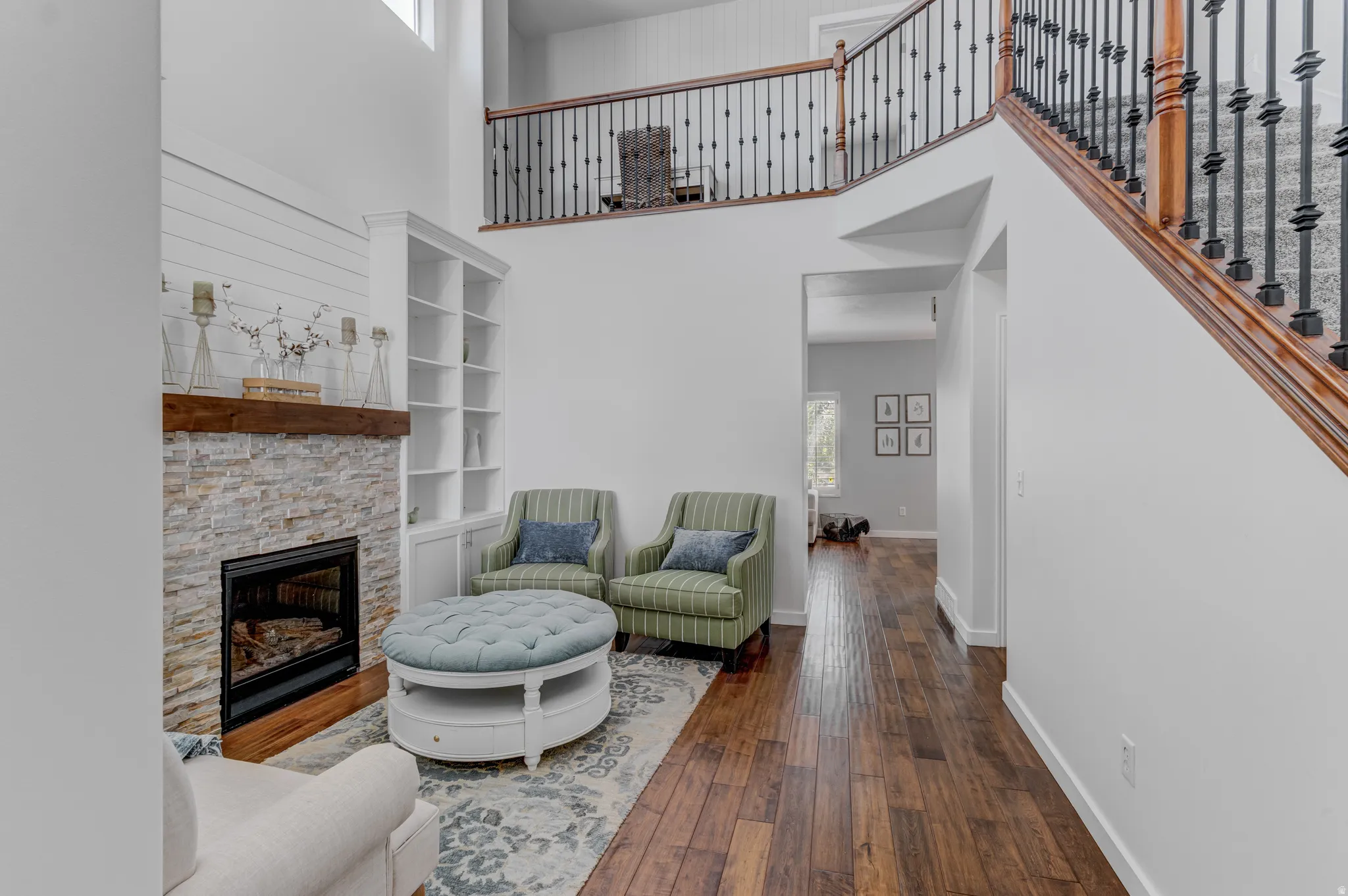 Two-story living area featuring a stone-faced fireplace with wood mantel, built-in shelving, and wood-finish flooring