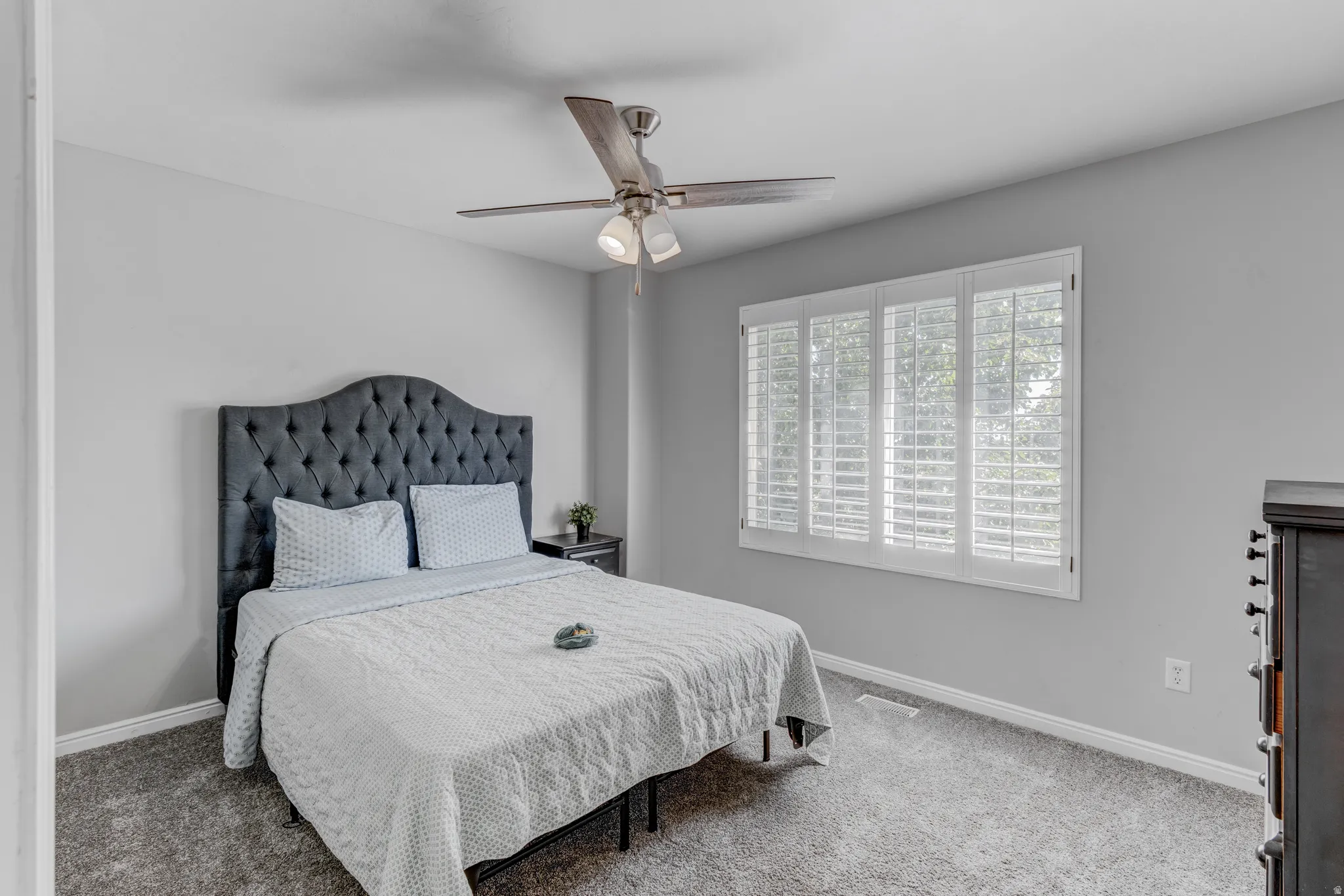 Ceiling fan with integrated lighting, window with white plantation shutters, and light gray wall paint