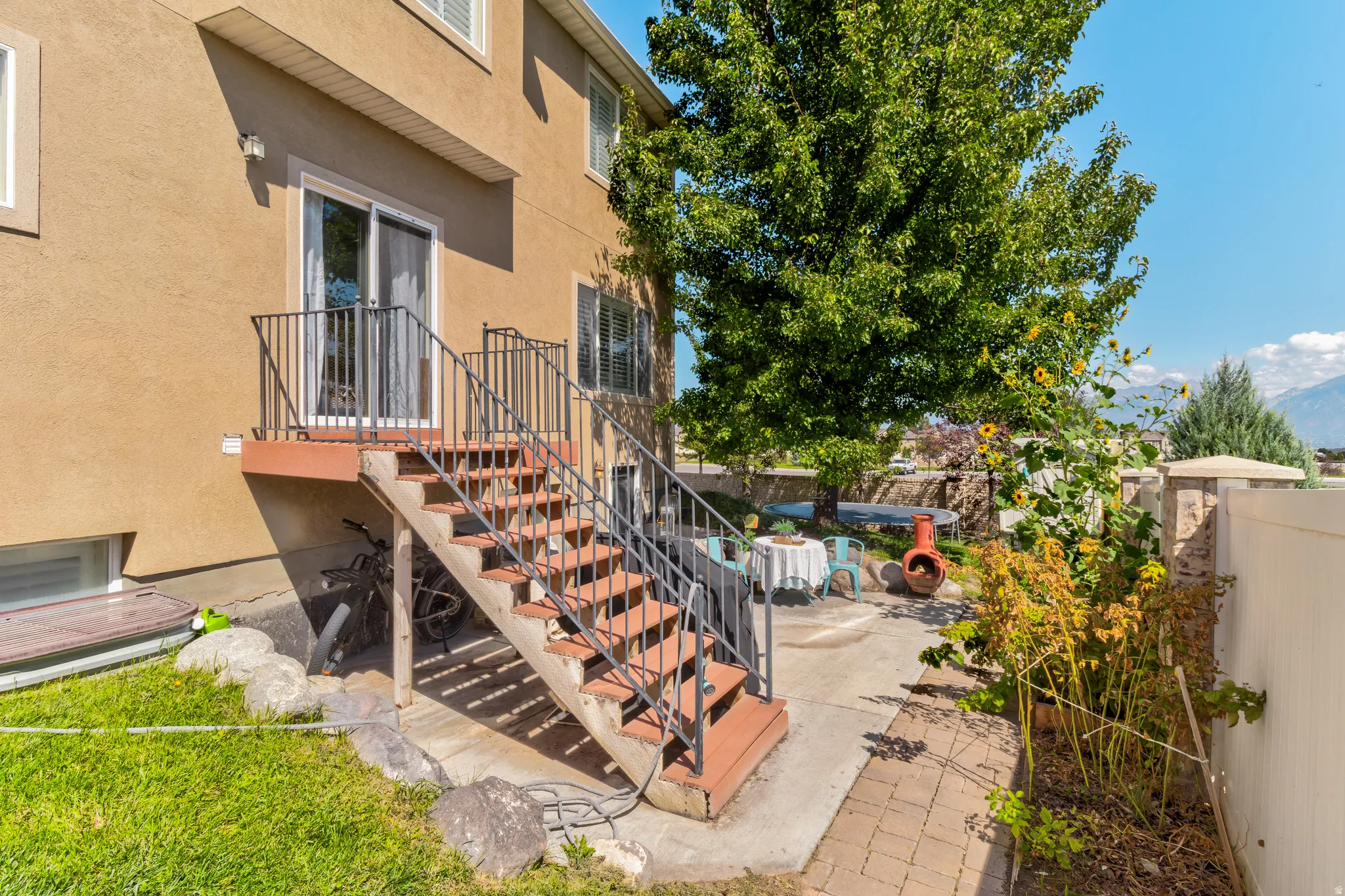 Stucco exterior with ground-level windows, a deck with metal railings, and exterior stairs leading to a concrete patio