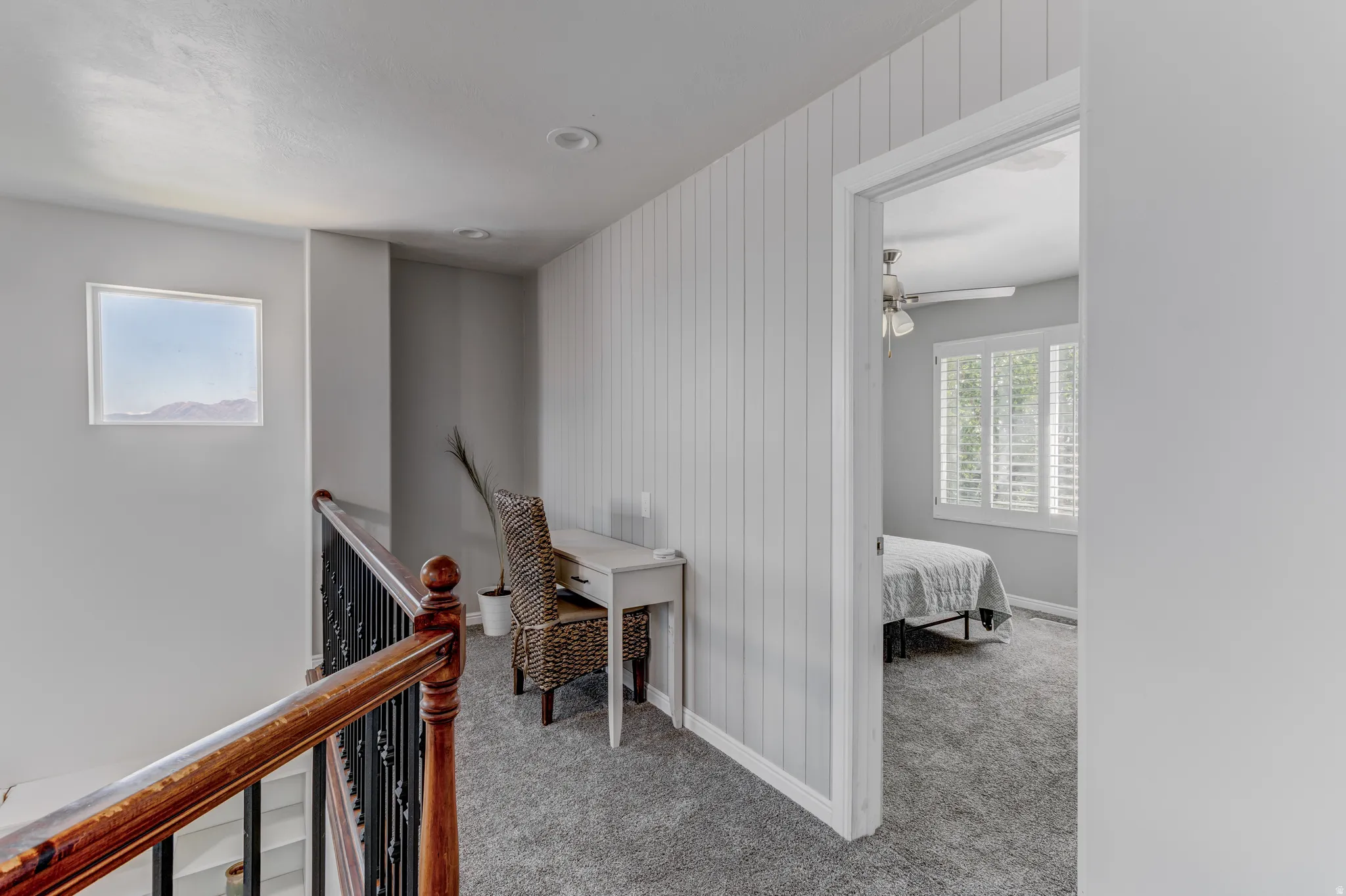 Hardwood railing with wrought iron balusters, recessed lighting, accent wall with vertical paneling, and a transom window