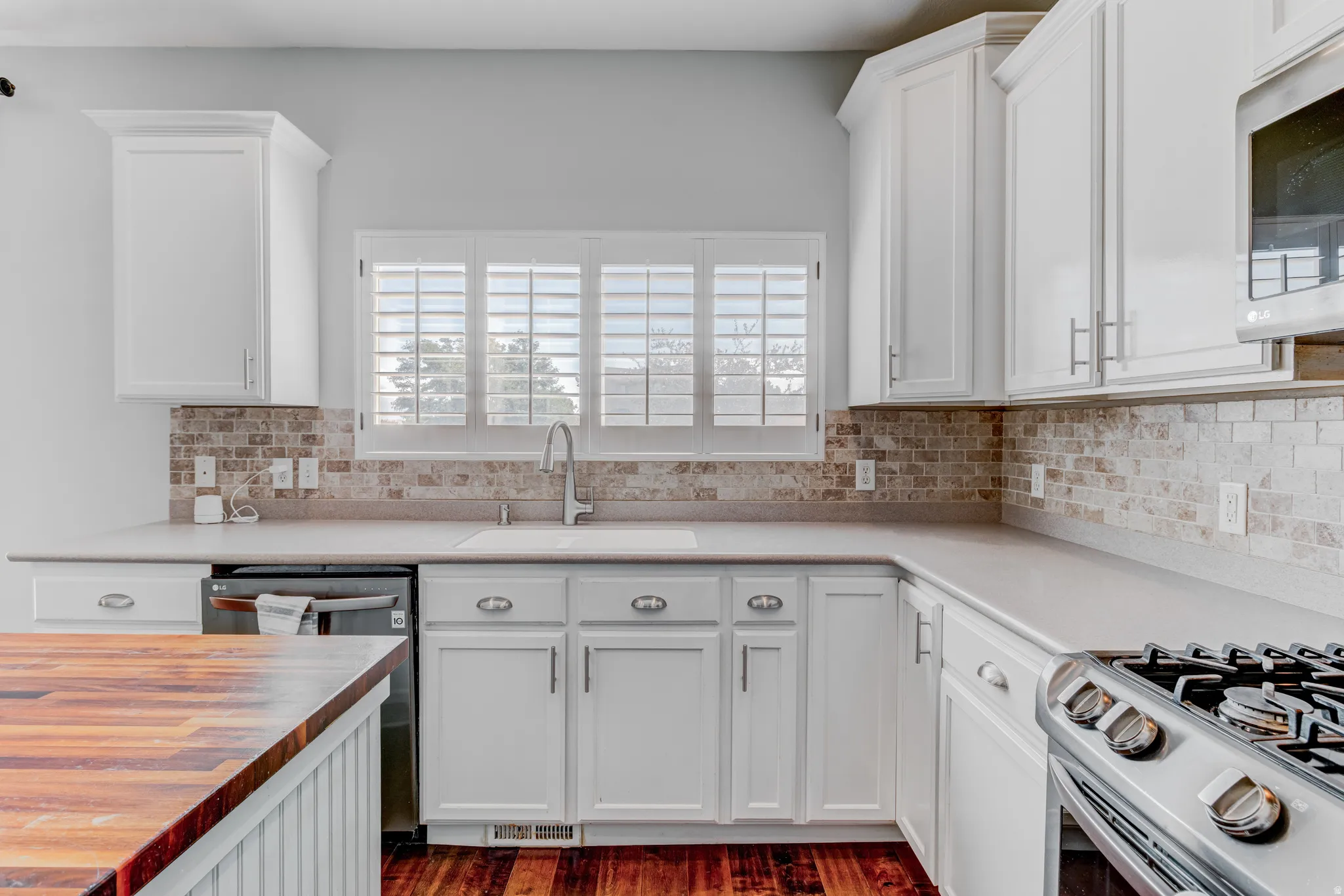 White cabinetry with brushed nickel hardware, stone tile backsplash, stainless steel appliances, and a wood-finish countertop island
