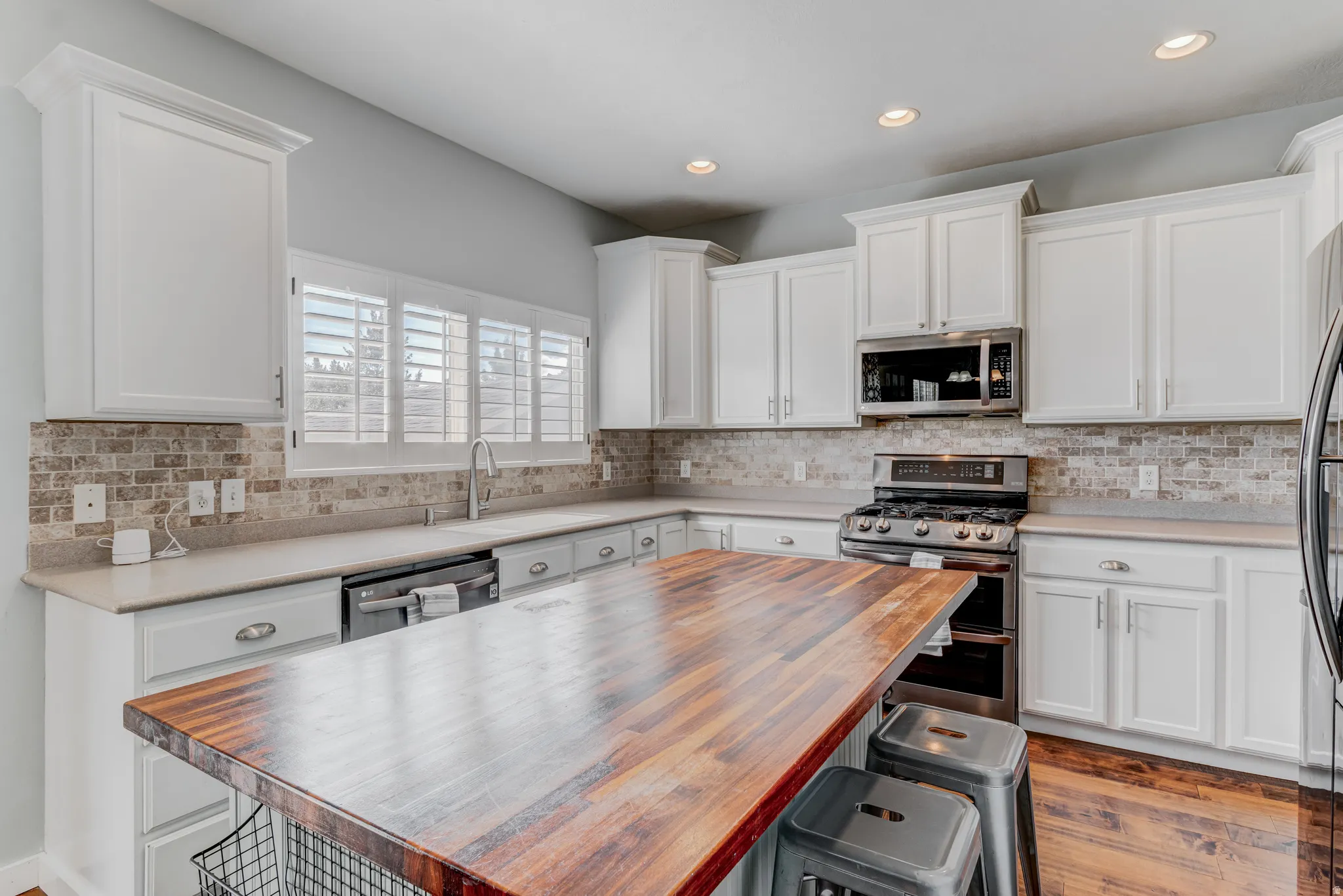 Kitchen featuring white cabinetry, stone countertops, a tile backsplash, stainless steel appliances, and a wood-finish island with seating