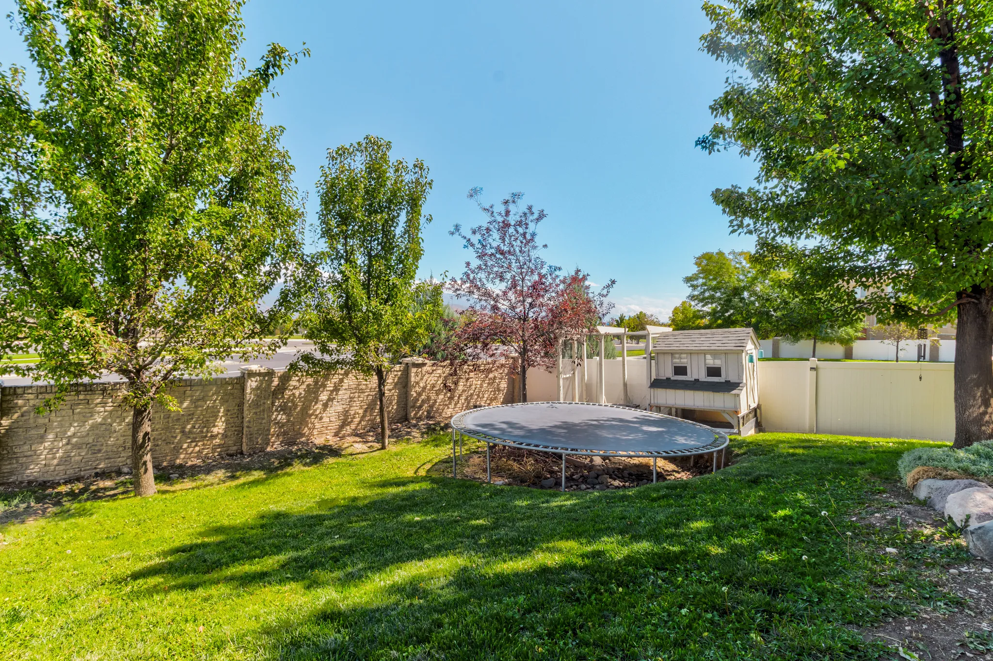 Expansive backyard featuring a manicured lawn, established trees, and a stone retaining wall