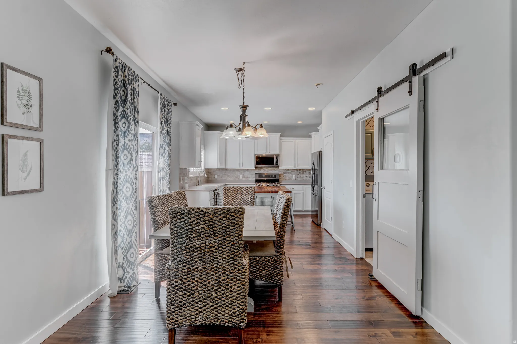 Wood-finish flooring throughout, modern kitchen with white cabinetry and stainless steel appliances, and a sliding barn door with frosted glass panel