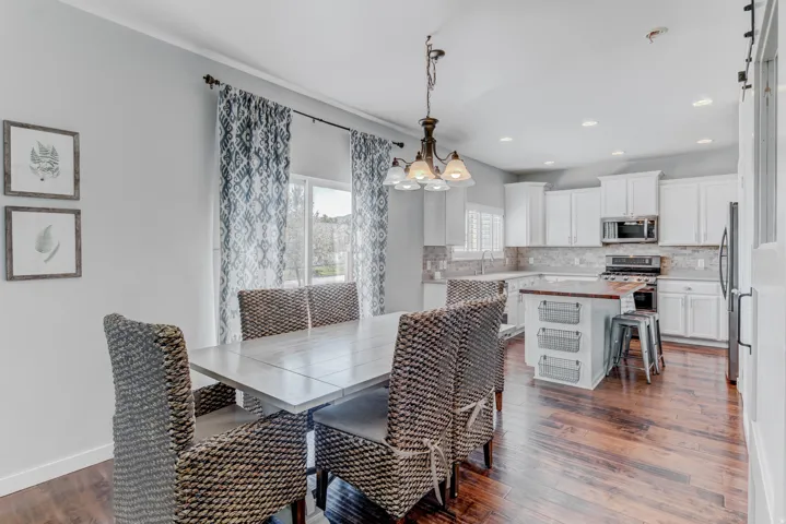 Wood-finish flooring, white cabinetry, integrated stainless steel appliances, recessed lighting, and a kitchen island with a wood countertop