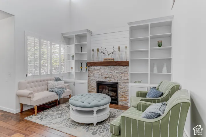 Stone-clad fireplace with wood mantel, flanked by built-in shelving, wood-finish flooring, and white plantation shutters