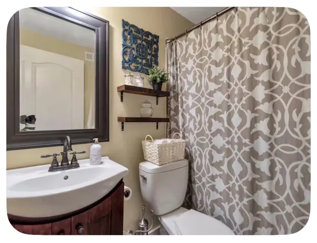 Bathroom featuring a wood-finish vanity with a white ceramic sink, a framed mirror, and wall-mounted shelving