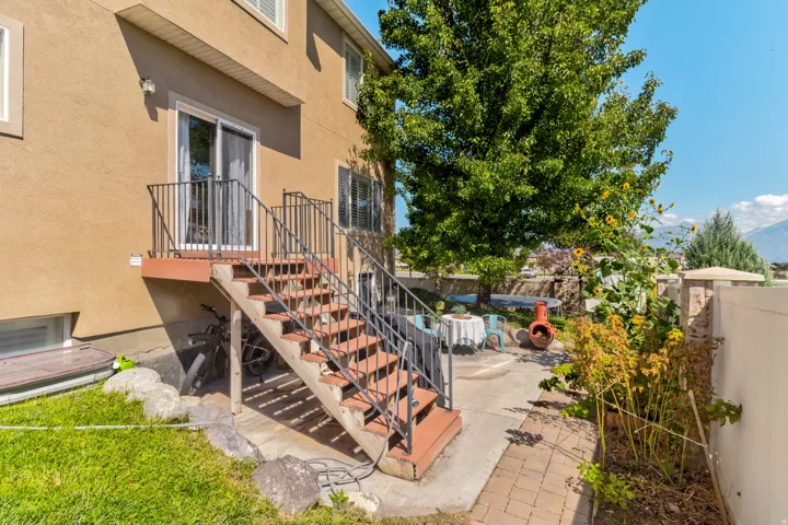 Stucco exterior with ground-level windows, a deck with metal railings, and exterior stairs leading to a concrete patio