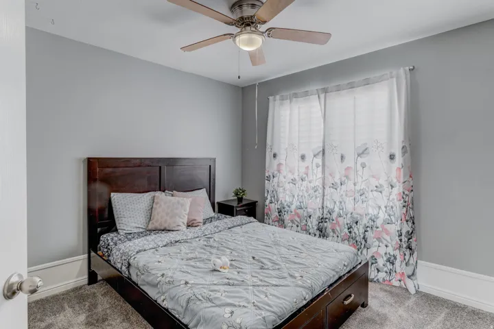 Gray wall paint with white trim, wood-finish bed frame, ceiling fan with integrated lighting, window with curtain rods