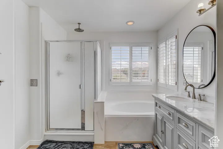 Bathroom featuring a built-in soaking tub, a separate glass-enclosed shower with a rainfall showerhead, a vanity with a stone countertop and an undermount sink, and plantation shutters