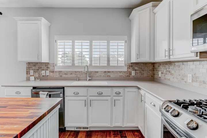 White cabinetry with brushed nickel hardware, stone tile backsplash, stainless steel appliances, and a wood-finish countertop island