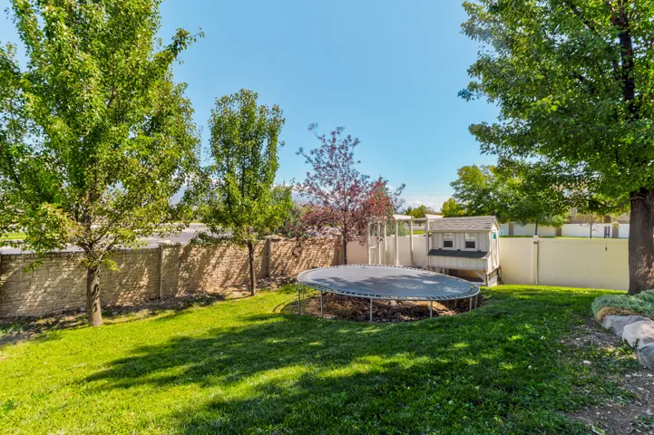 Expansive backyard featuring a manicured lawn, established trees, and a stone retaining wall