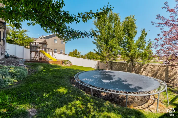 Expansive backyard featuring a manicured lawn, established trees, and a privacy fence