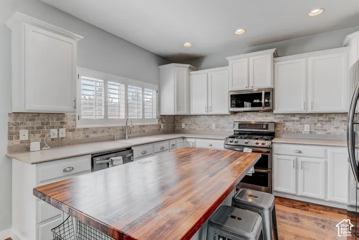 Kitchen featuring white cabinetry, stone countertops, a tile backsplash, stainless steel appliances, and a wood-finish island with seating