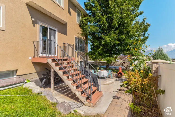 Stucco exterior with ground-level windows, a deck with metal railings, and exterior stairs leading to a concrete patio