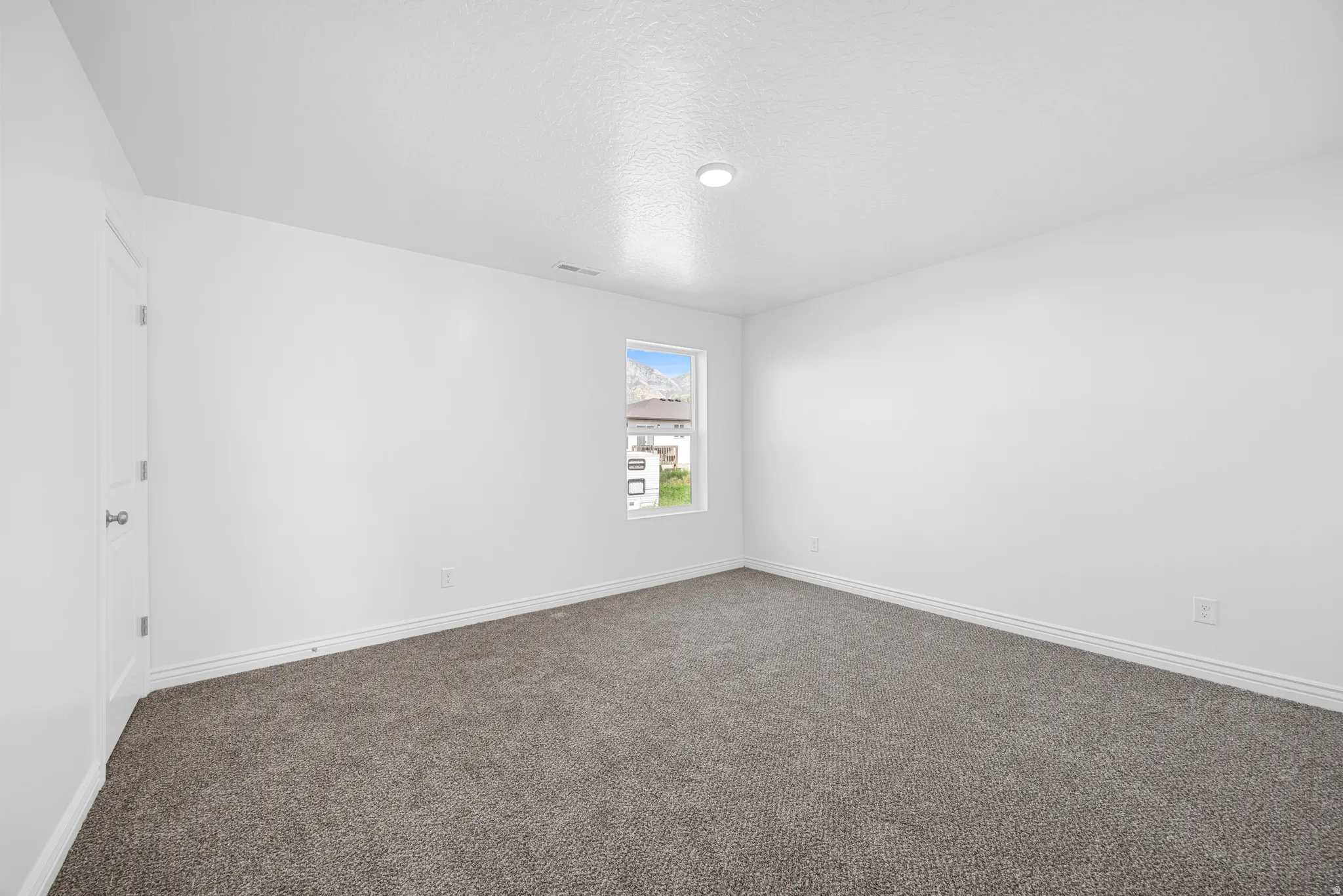 Spacious room with plush gray carpeting, white walls, and a single window offering exterior scenery