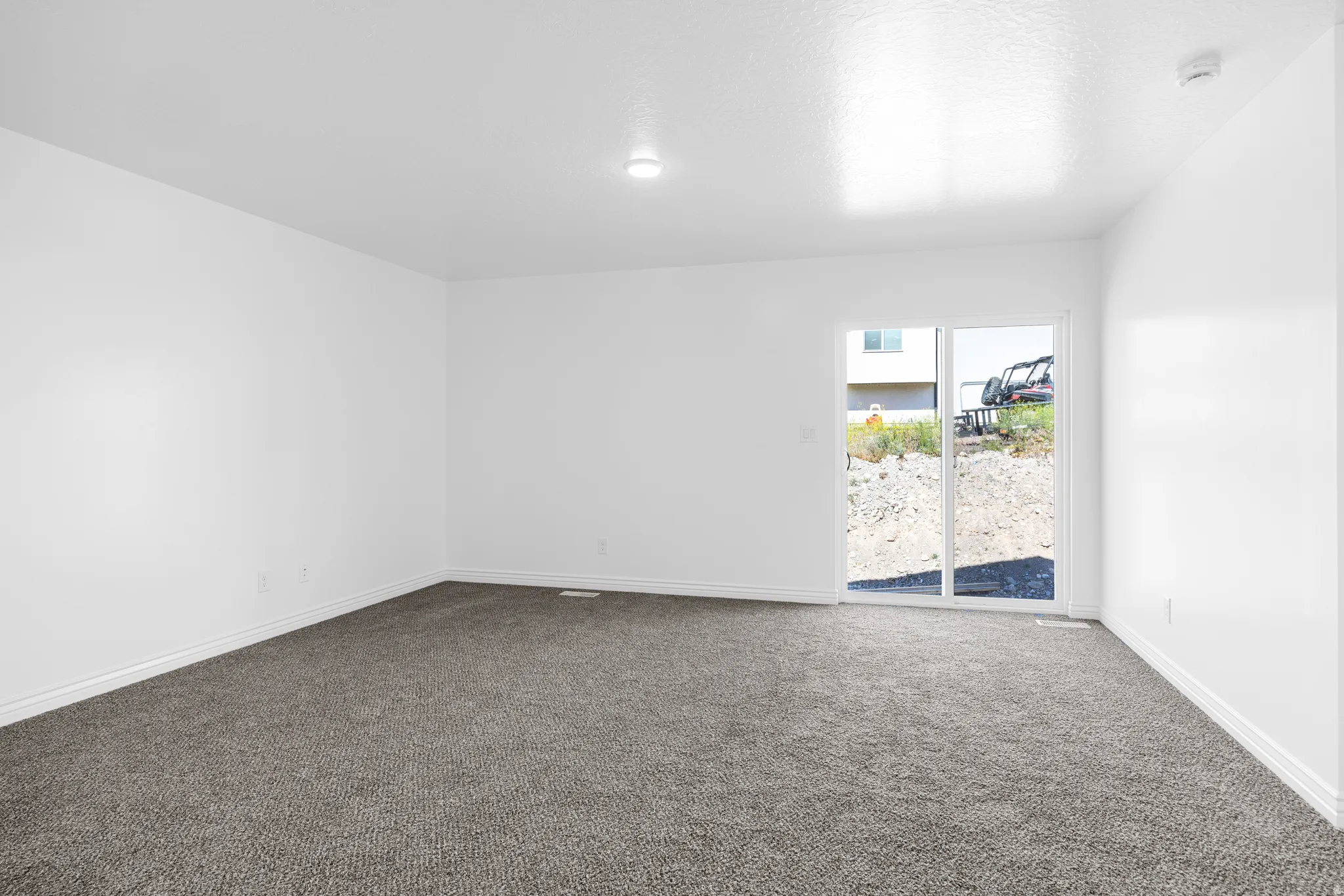 Spacious room featuring neutral carpeting, white walls, a recessed ceiling light, and a sliding glass door