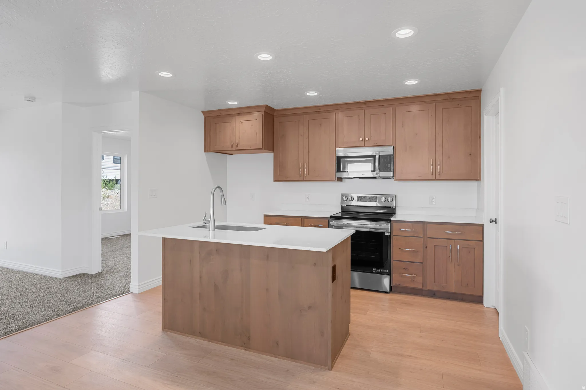 Kitchen featuring wood-finish flooring, recessed lighting, wood cabinetry, stainless steel appliances, and a central island with a sink