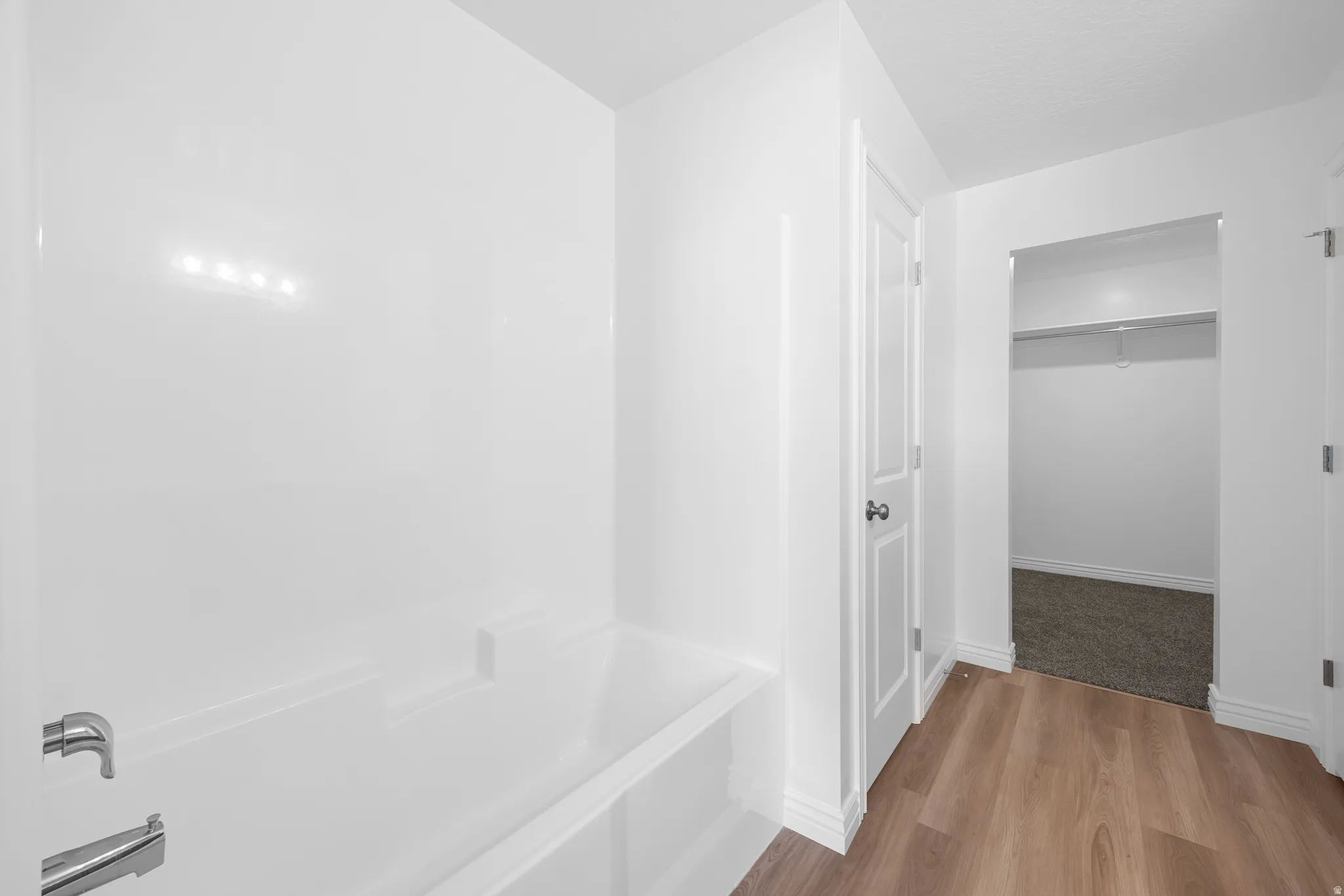White acrylic bathtub and shower surround with chrome fixtures, wood-finish flooring, and a white two-panel door