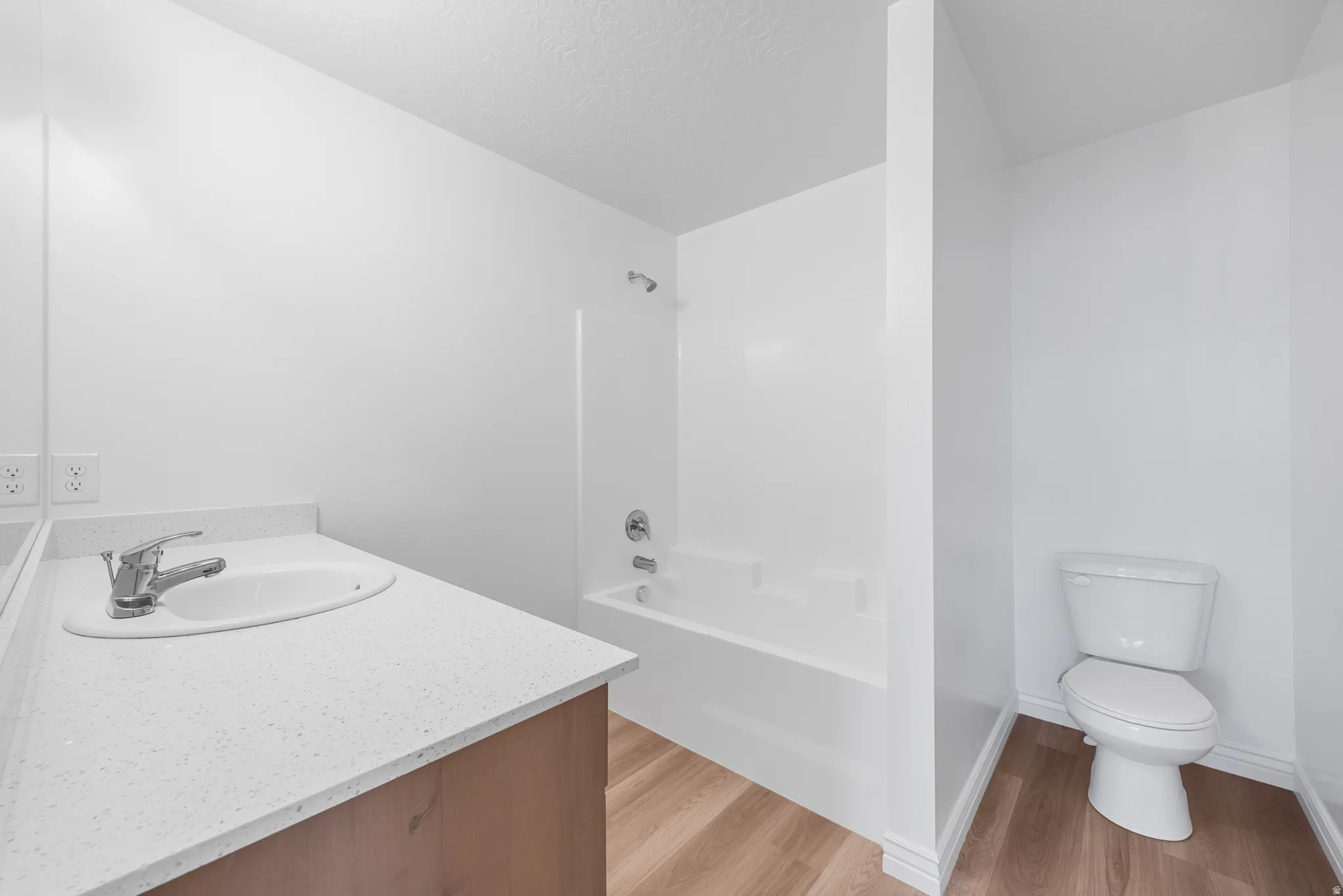 White vanity with integrated sink, chrome faucet, white bathtub with shower, toilet, and wood-finish flooring