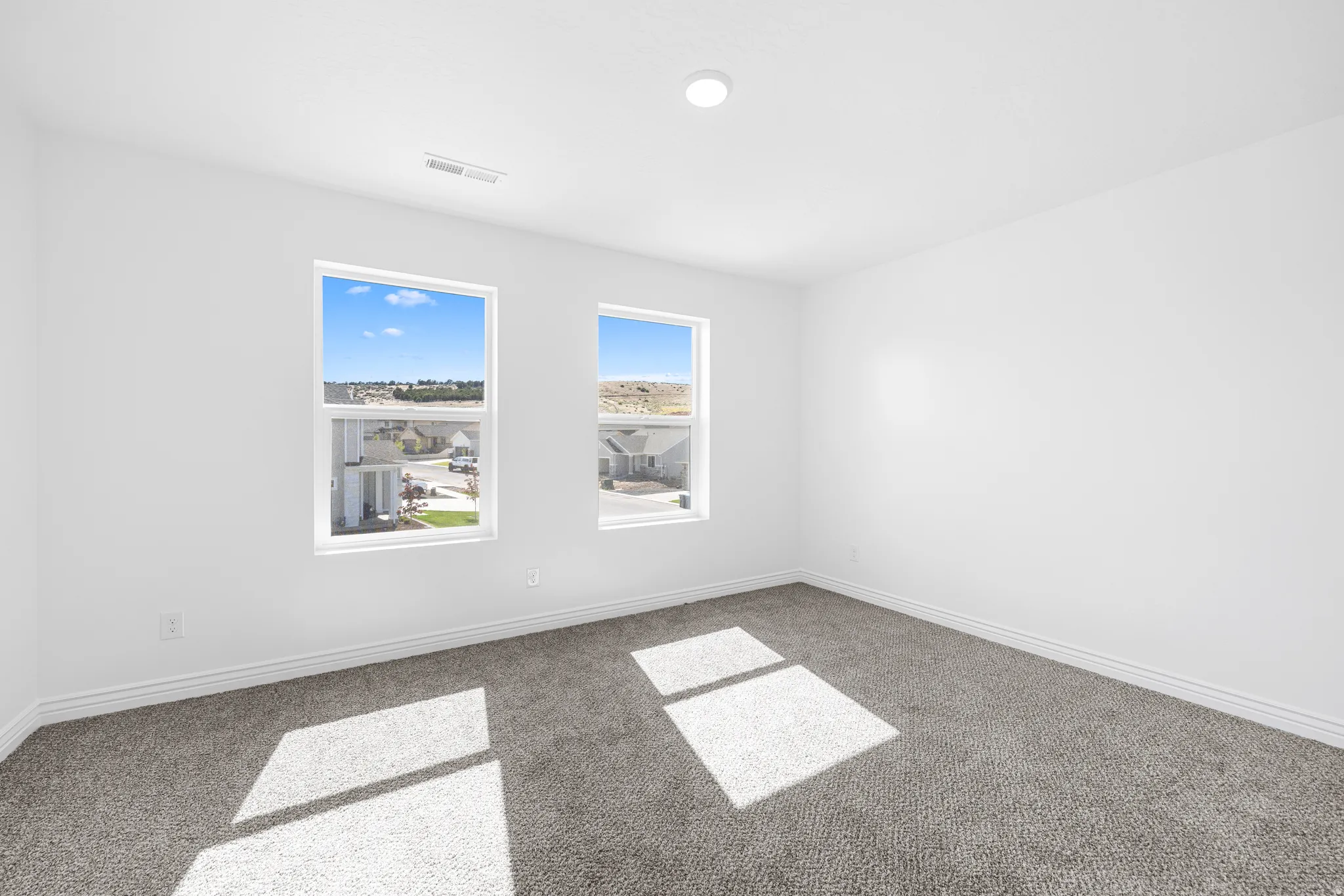 Two large windows, recessed ceiling light, and gray carpeting