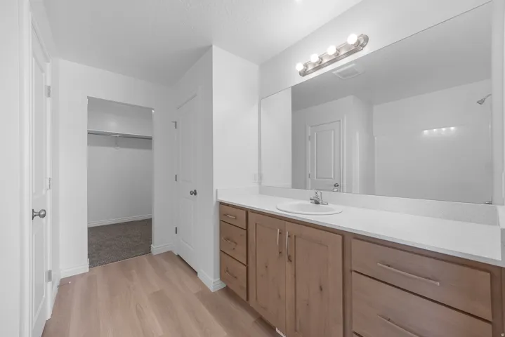 Wood-finish flooring, white solid-surface countertop, wood-finish vanity with ample storage, large vanity mirror, and modern vanity lighting