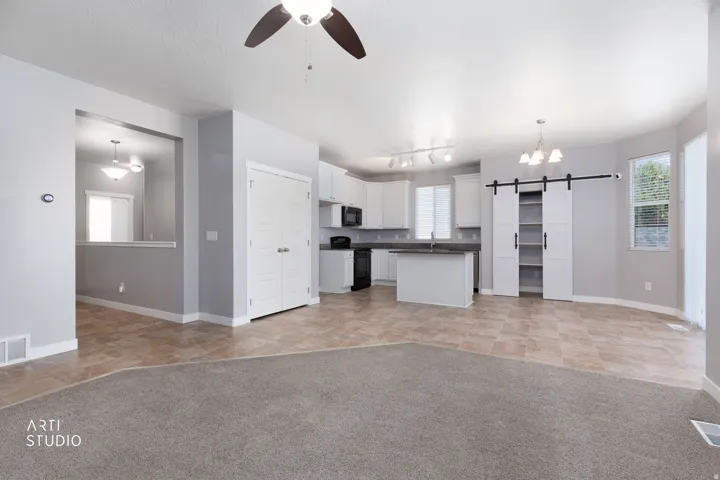 Open-concept living area featuring a kitchen with white cabinetry, a kitchen island, integrated black appliances, and track lighting