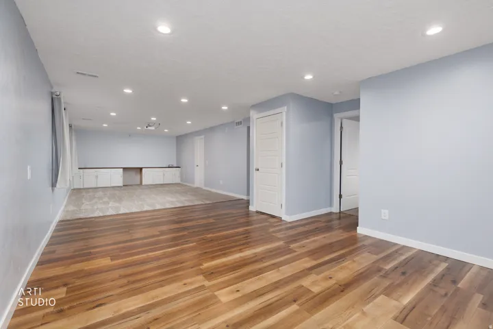 Recessed lighting, wood-finish flooring, light blue wall paint, built-in cabinetry with dark countertops, and a projector