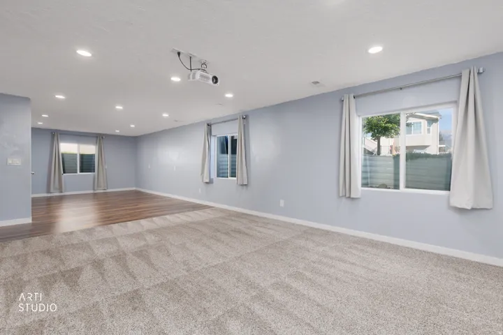 Expansive room featuring recessed lighting, a ceiling-mounted projector, and two distinct flooring types