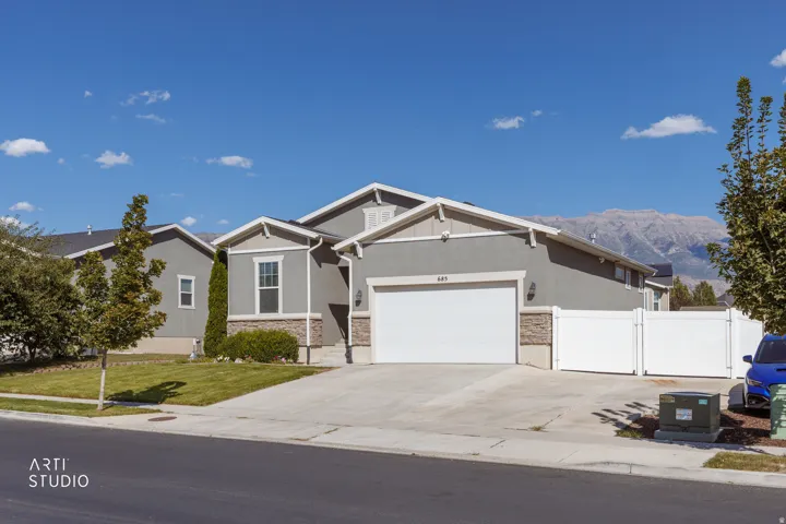 Gray stucco exterior with stone accents, attached two-car garage, white privacy fence, concrete driveway, and a manicured lawn