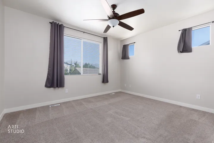 Plush gray carpeting, multiple windows providing natural light, and a ceiling fan with integrated lighting