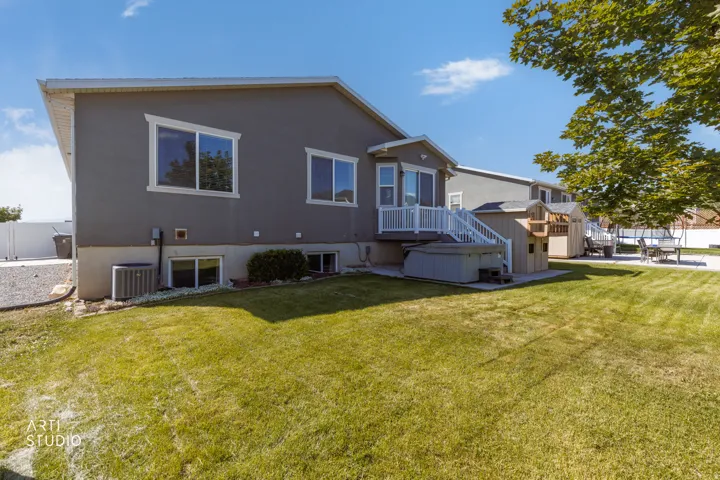 Expansive green lawn with a gray stucco exterior, white window trim, and a raised white deck