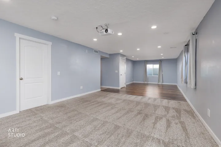 Recessed lighting, ceiling-mounted projector, wood-finish flooring, light-toned carpeting, and a window with light-filtering blinds