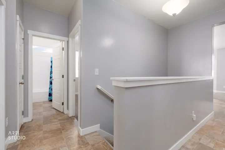 Hallway featuring neutral-toned walls, tile flooring, white trim, and an overhead light fixture