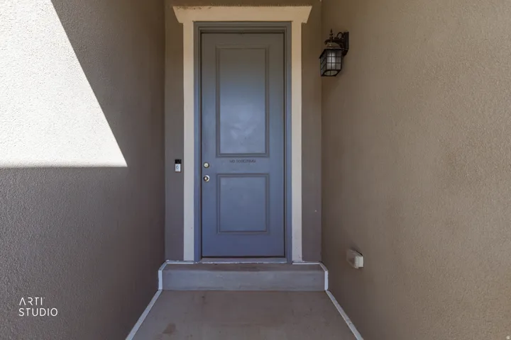 Recessed entry with a paneled door, decorative exterior sconce, and stucco finish