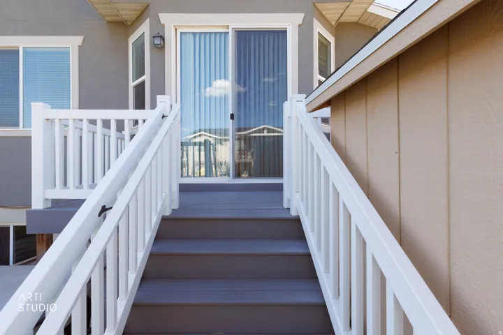 Exterior staircase with white railings, grey composite decking, and a sliding glass door entry