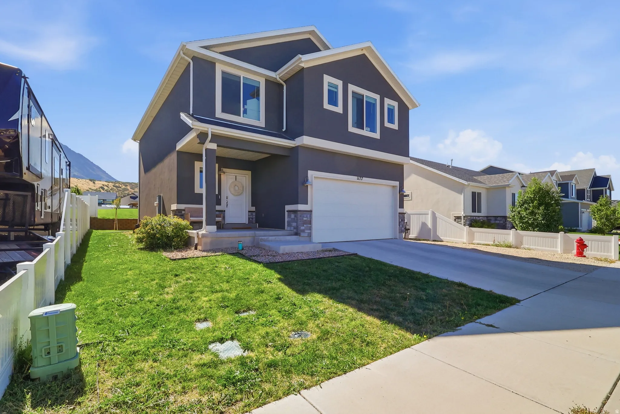 Contemporary gray stucco exterior with white trim, covered front porch, attached garage, concrete driveway, and front lawn
