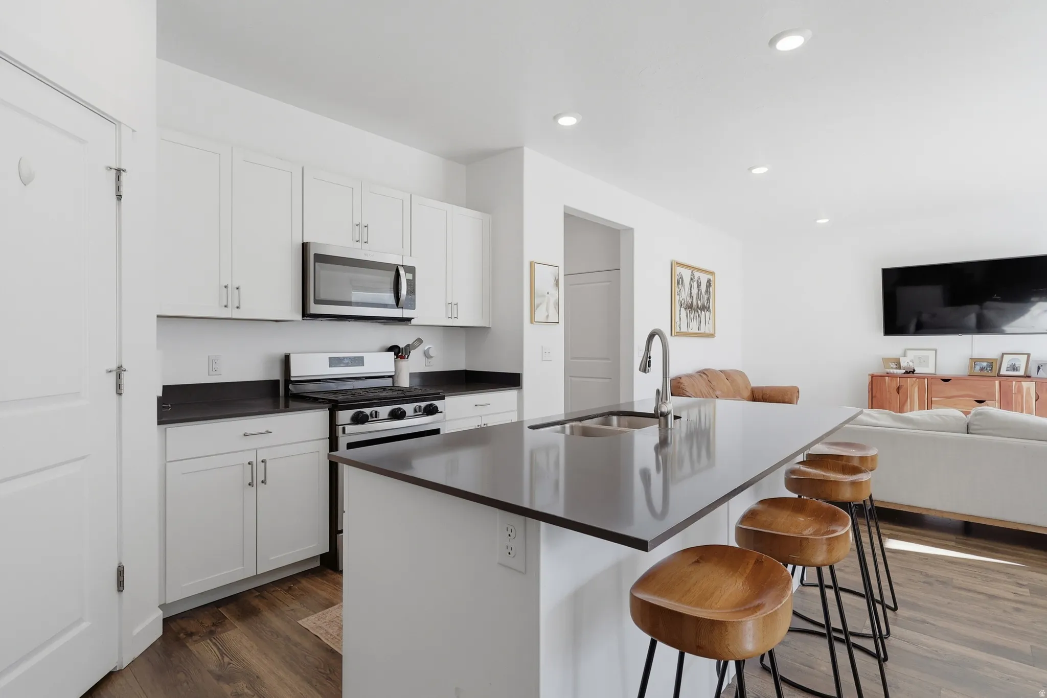 Recessed lighting illuminates a kitchen featuring white cabinetry, dark countertops, and stainless steel appliances