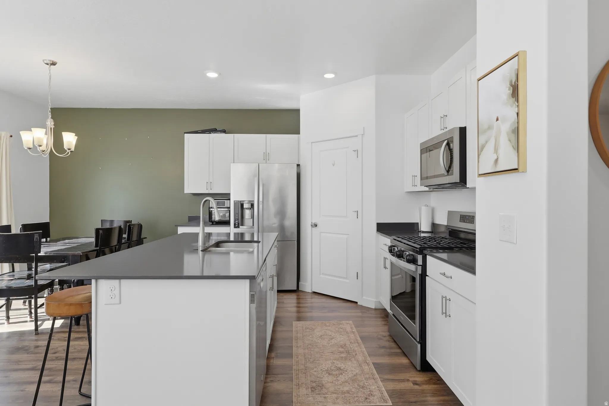 Kitchen featuring a central island with an undermount sink, white cabinetry, dark countertops, and stainless steel appliances